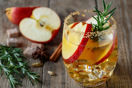 Apple drink with apple slices in a glass, a sprig of rosemary and brown sugar on the rim of a glassの写真素材