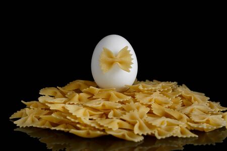 Pasta bows on a black background and a white egg on top, symbolizing the content of eggs in pastaの写真素材