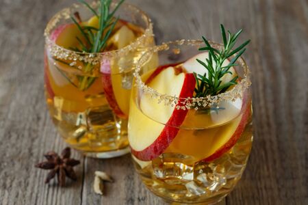 Apple drink with apple slices in a glass, a sprig of rosemary and brown sugar on the rim of a glassの写真素材