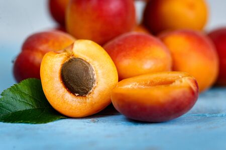 A bunch of ripe apricots on a wooden background, painted in blue, with a cut berry in frontの写真素材