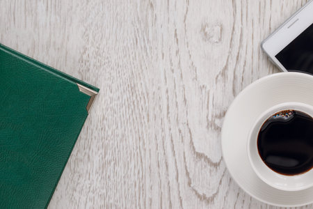 Business still life with a cup of coffee, a telephone on a wooden light surface