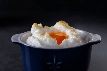 Delicate baked egg Orsini (eggs in the cloud). French breakfast in a blue cocotte against a dark backgroundの写真素材