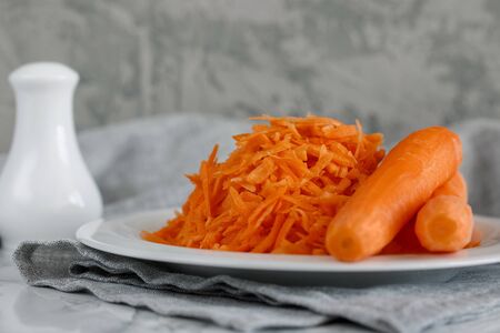 Grated carrots on a white plate and two whole carrots nearbyの写真素材