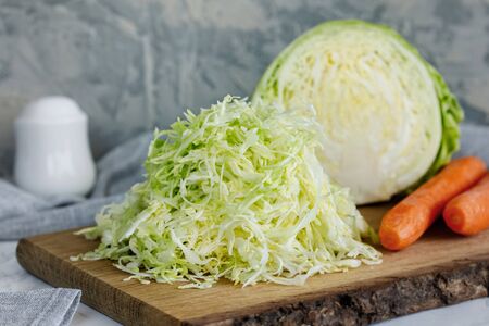 Fresh young shredded cabbage on a wooden board and half a cabbage and carrots nearbyの写真素材