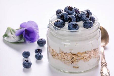 Thick yogurt with oatmeal in a glass jar decorated with fresh blueberries, light breakfastの写真素材