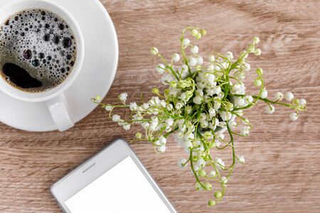 A bouquet of lilies of the valley on a table with a cup of coffee and a telephone. View from aboveの写真素材