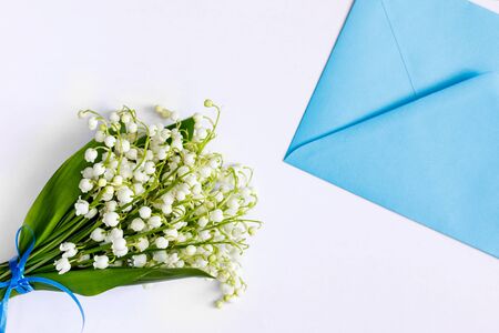 Bouquet of lilies of the valley and a blue envelope on a white tableの写真素材