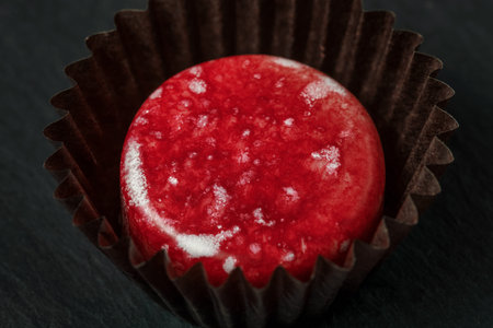 Red colored luxury handmade chocolate candy on black background. Exclusive handcrafted bonbon....