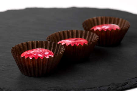 Red colored luxury handmade chocolate candy on black background. Exclusive handcrafted bonbon. Product concept for chocolatier. Fashion foodの写真素材