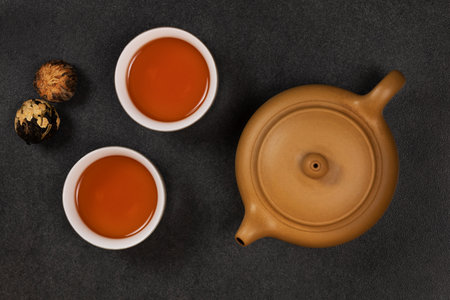 Yellow-orange tea in clay cups against the background of a ceramic teapot and Chinese tea balls. view from above.の写真素材