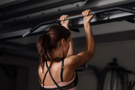 Cute young muscular girl doing pull-ups exercise at the gym.