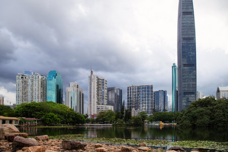 A park alley in the center of Shenzhen overlooking a lotus pond and a cityscape with skyscrapers.の写真素材