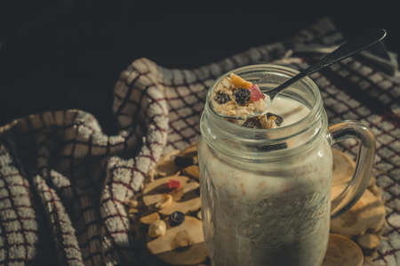 Glass jar with a healthy breakfast of oatmeal with nuts, dried fruits and yogurt. Early morning, side view, close upの写真素材
