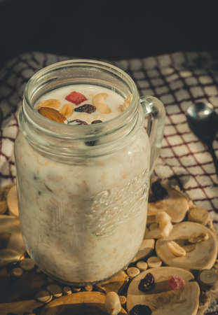 Glass jar with a healthy breakfast of oatmeal with nuts, dried fruits and yogurt. Early morning, side view, close upの写真素材