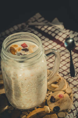 Glass jar with a healthy breakfast of oatmeal with nuts, dried fruits and yogurt. Early morning, side view, close upの写真素材
