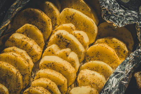 Slices of potatoes in marinade and spices. Potatoes in foil for baking in the oven. Cooking. Selective focusの写真素材