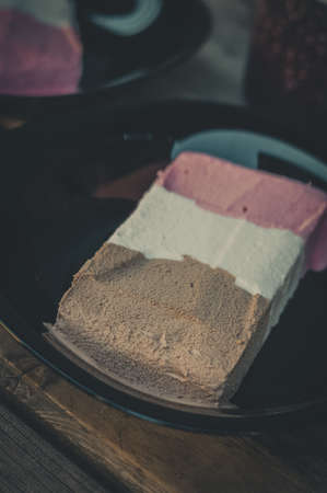 Blurred ice cream in black plates and on a wooden table. Chocolate, strawberry and vanilla ice cream. Portions of ice cream. Selective focus, blur, grainの写真素材