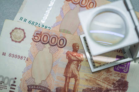Verification of Russian banknotes for authenticity under a magnifying glass. Used money. Selective focusの写真素材