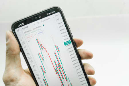 A chart of financial exchange quotes on a smartphone screen in hand. Trading on the stock exchange from a mobile phone. Close-up, selective focusの写真素材