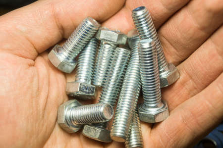 A handful of metal bolts. Fasteners in the palm of your hand. Close-up of the hardware in the hand. Soft focusの写真素材