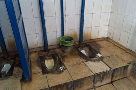 Dirty public toilet. Not a hygienic mens restroom. An old-style toilet is built into the floor. Soft focus, selective focus.の写真素材