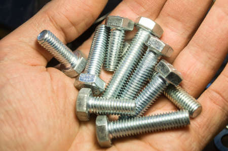 A handful of metal bolts. Fasteners in the palm of your hand. Close-up of the hardware in the hand. Soft focusの写真素材