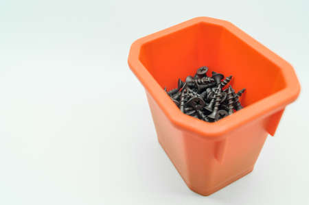 Black screws in orange box. Placer of metal fasteners. Close-up of short screws. Selective focus, isolated on whiteの写真素材