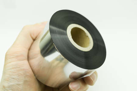 Single thermal transfer ribbon in hand. Wax thermo ribbon on cardboard reel for barcode. Supply material for printing industry. Selective focus, isolated on whiteの写真素材