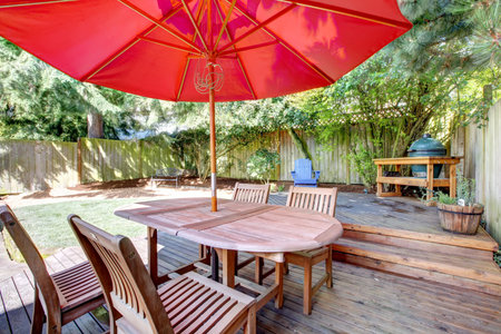 Back yard large deck with red umbrella and chairs and fenced yard.