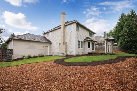 Large beige house with empty backyard during spring with mulch and grass.の写真素材