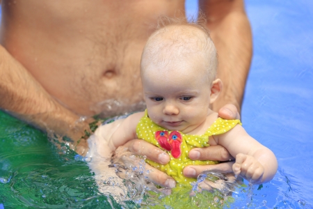 Small baby girl is swimming in the pool with daddy for the first time. Three months old baby.の写真素材