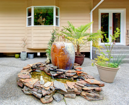 Backyard porch with concrete floor and decorated rocks with big ceramic vase, flower pots with palm
