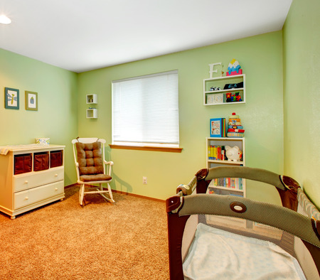 Green and beige cozy nursery room with baby crib, rocking chair and wooden cabinetの写真素材