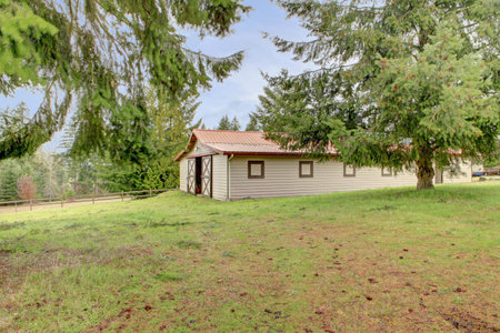 Fenced countryside horse stable barn with fir trees.