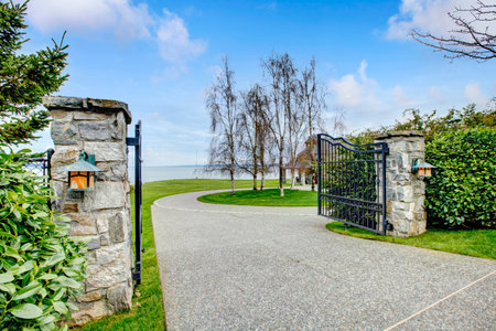 Entrance iron gates with stone columns. View of driveway and roundabout.