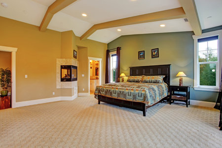 Spacious master bedroom with high coffered ceiling, beige carpet floor and fireplace built in the...