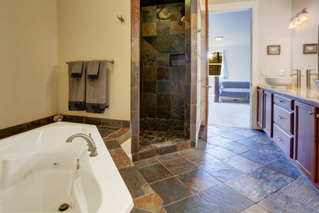 Bathroom interior with dark tile floor and tile shower trim. View of bathroom vanity cabinet with...
