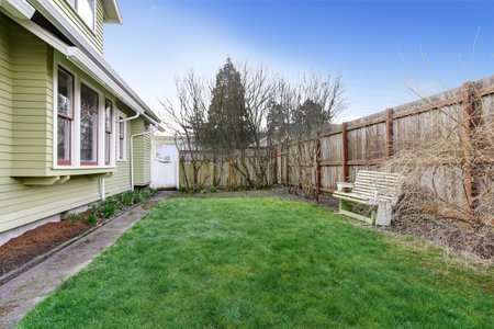 House with small backyard. View of high fence and old bench. Early spring