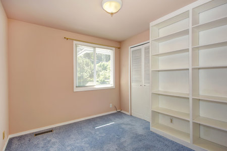 Empty room interior in soft peach color with light blue carpet floor and white bookshelfの写真素材