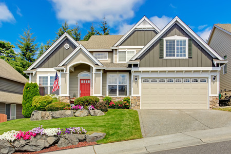 Grey house exterior with entrance porch and red door. Beautiful front yard landscape with vivid flower and stones Grey house exterior with entrance porch and red door. Beautiful front yard landscape with vivid flower and stones