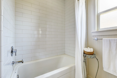 Simple bathroom with tile wall trim and bath tub, white curtains and stand with wicker basket for towelsの写真素材