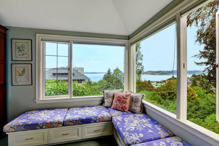 Cozy sitting area in bedroom with bay view. Bench with drawers and purple floral pillows create comfort in bedroomの写真素材