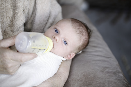 Baby drinking milk from bottle with nipple in mouthの写真素材