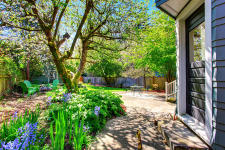 Fenced backyard with lots of greenery, trees and concrete patio area. View of the blue shed.