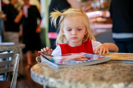 Sweet little blond girl looks magazine in a cafe, Christchurch, New Zealandの写真素材