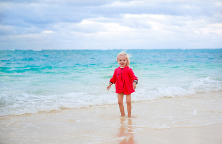 Little girl in red coat staying in the water on the beach with blue water background. Oahu , New Zealandの写真素材