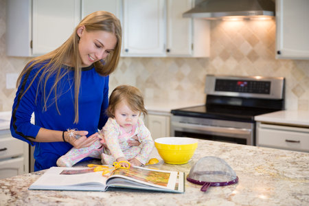 Young beautiful caucasian woman with cute baby girl cooking together, having fun in the kitchenの写真素材
