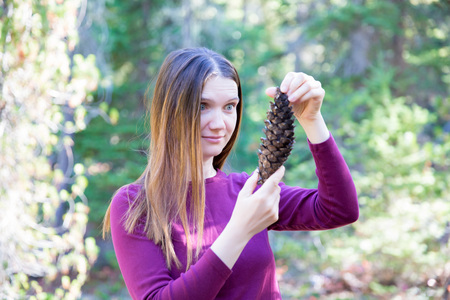 Young pretty woman with surprised look holding big pinecone found in the forestの写真素材