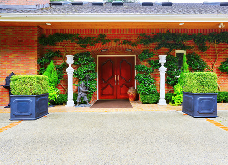 Luxury house entrance overgrown with green plants front double door of solid wood, also decorated with nice vase and man's statue of a warrior. Northwest, USAの写真素材