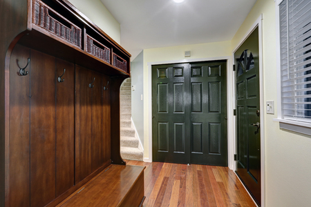 Entrance foyer features pale yellow walls, built-in closet with dark green doors, wood bench with open shelves filled with wicker storage baskets  and hardwood floor. Northwest, USAの写真素材